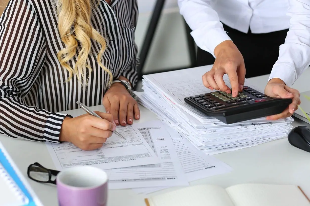 Two people are working on papers and a calculator.