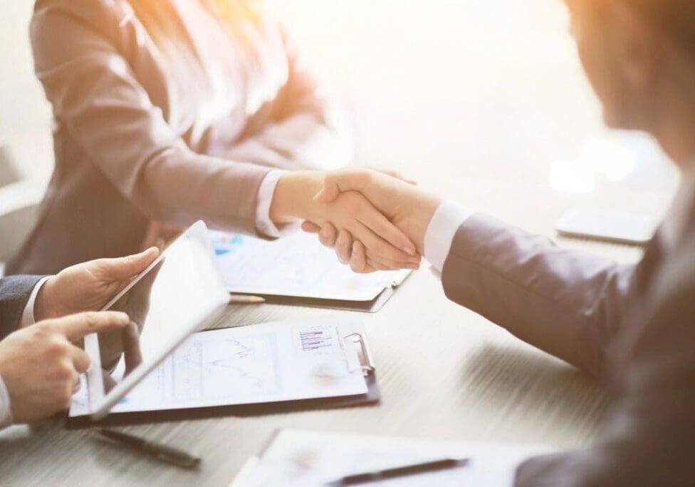 Two people shaking hands over a table.